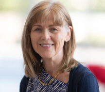 A headshot of Professor Anne Rosser. She has medium legnth brown hair and is smiling at the camera, wearing a blu top and a navy cardigan.