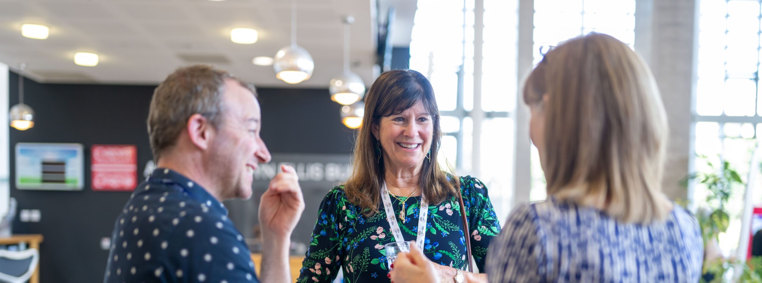 Three people standing chatting to each other, two women and one man.